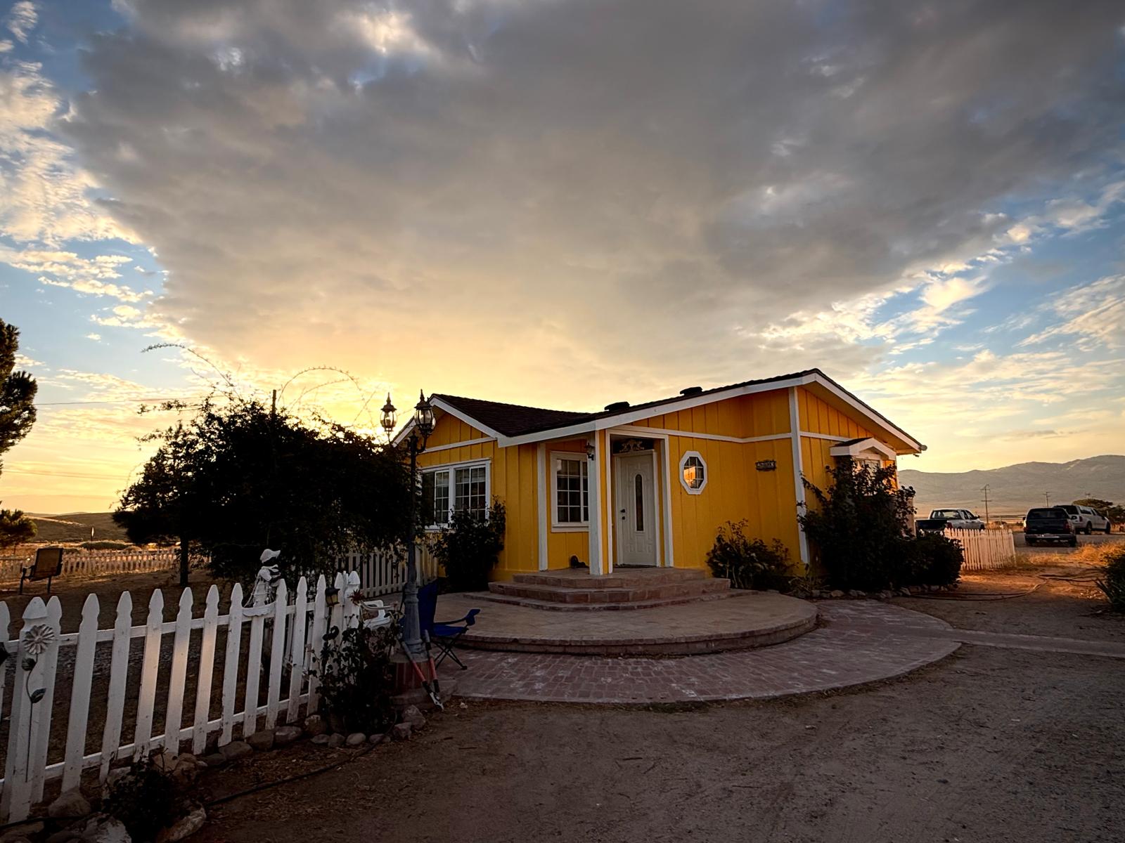 The yellow ranch house behind its white picket fence at sunset